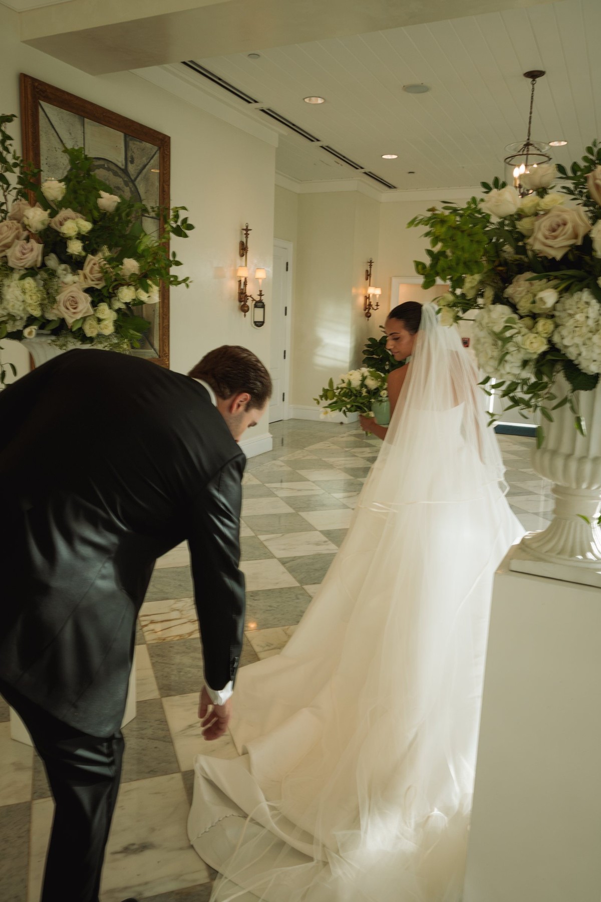 Groom fixing the bride's train in the flower filled ceremony room at Rosewood Bermuda
