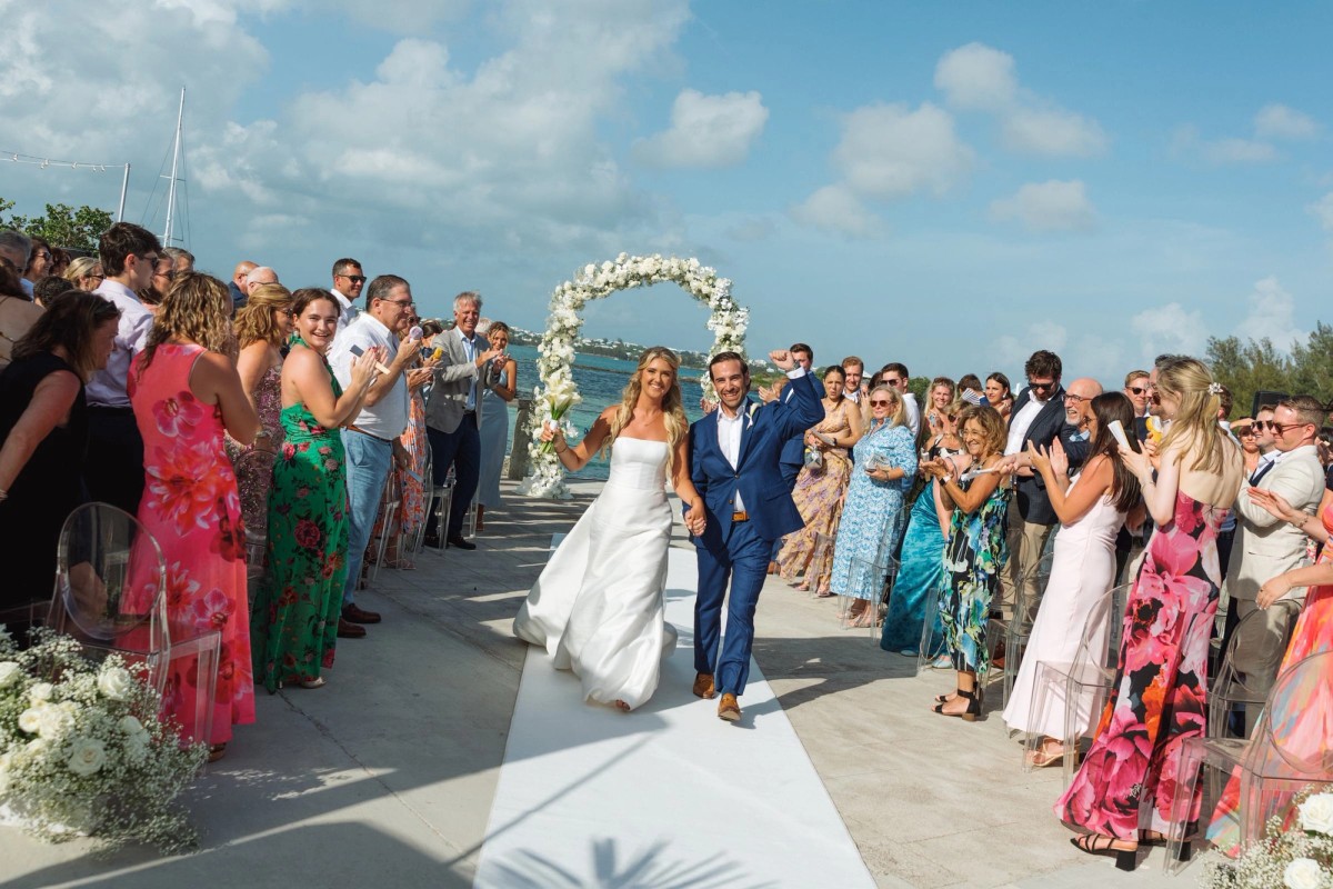 Guests cheer as the newlyweds walk up the aisle from the floral arch on Hawkins Island, Bermuda