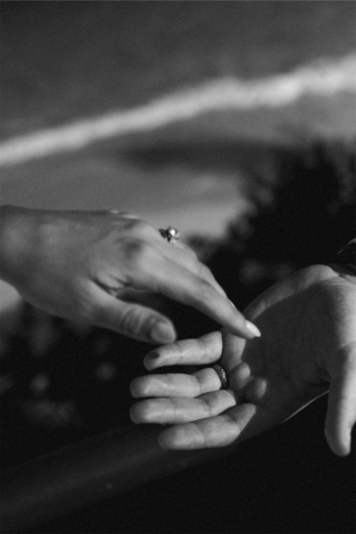 Black and white close-up of the couple's linked hands with the ring showing