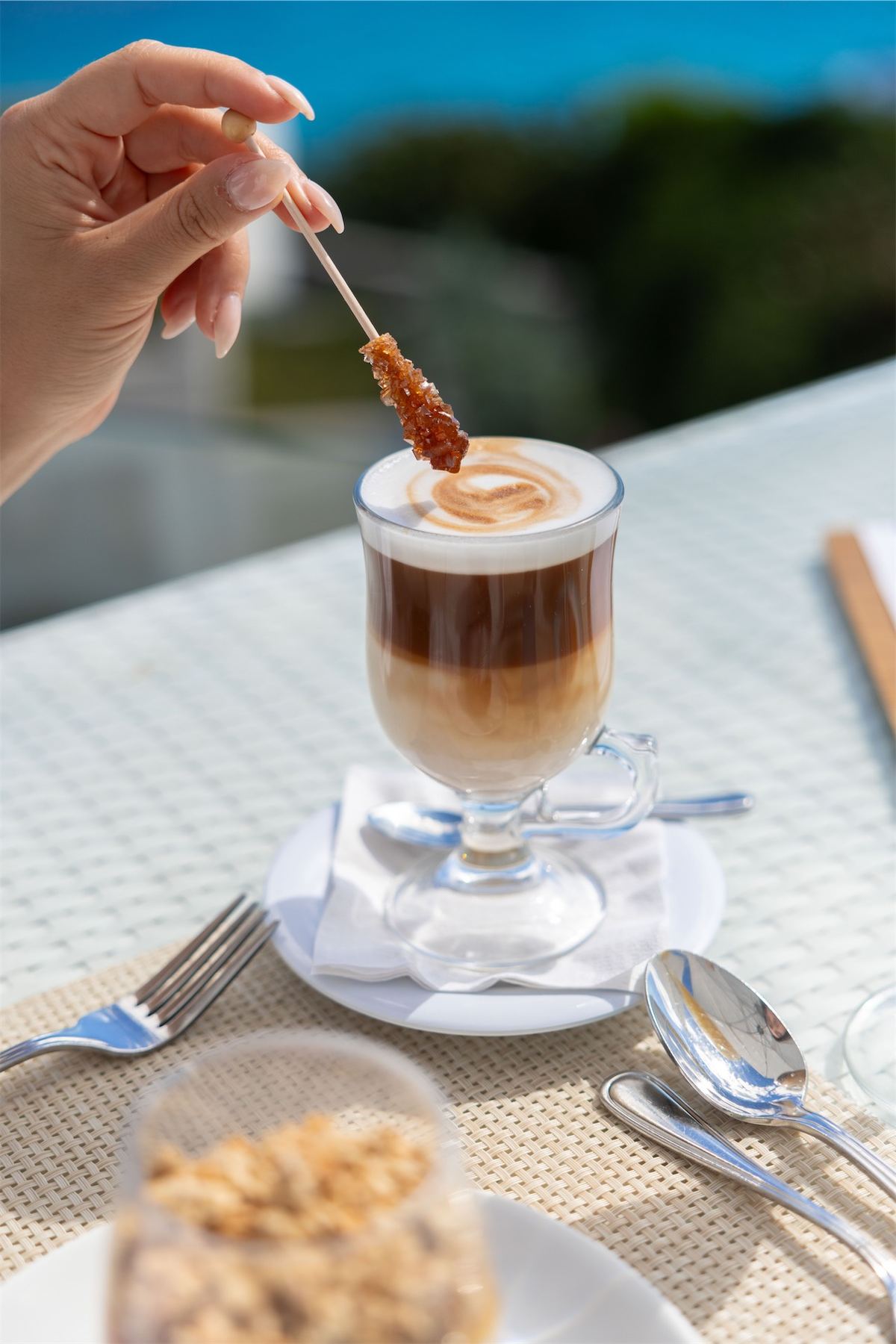 Hand lifting a biscotti from a layered latte on an ocean-view breakfast table