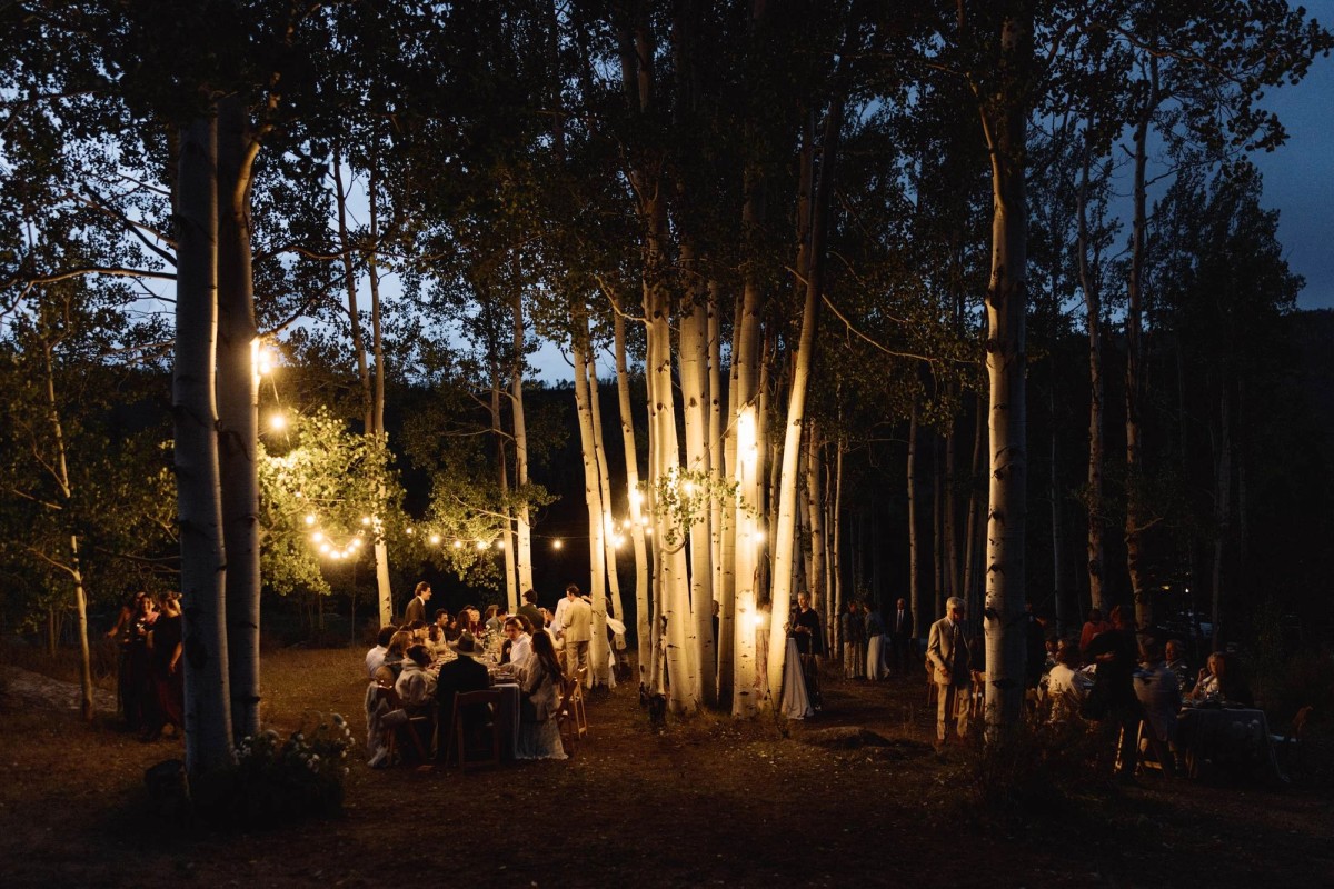 String lights glow through the aspen grove as the reception carries on into blue hour at a mountain ranch among the aspens