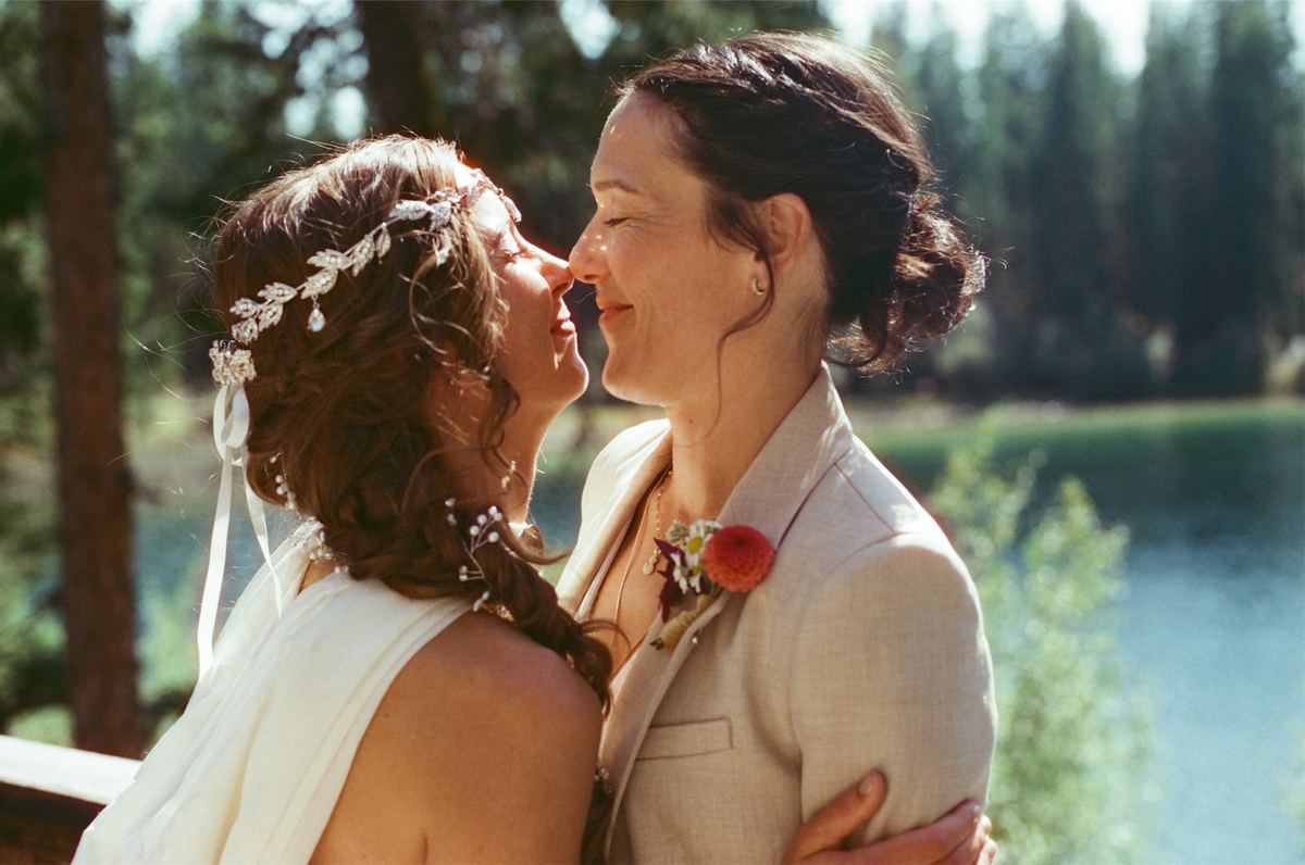 Two brides leaning in nose to nose on the lakeshore