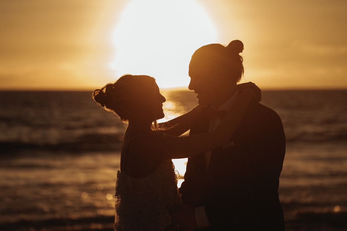 Couple silhouette embrace at sunset on the beach, golden hour wedding photography