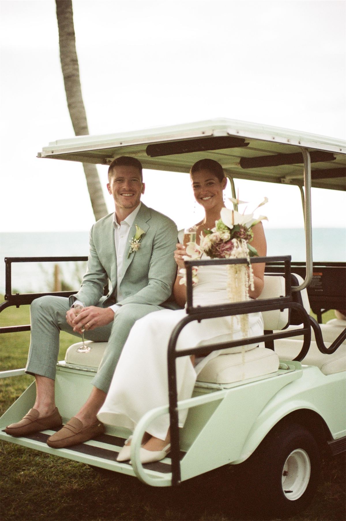 Bride and groom riding a golf cart along the shoreline path after the ceremony