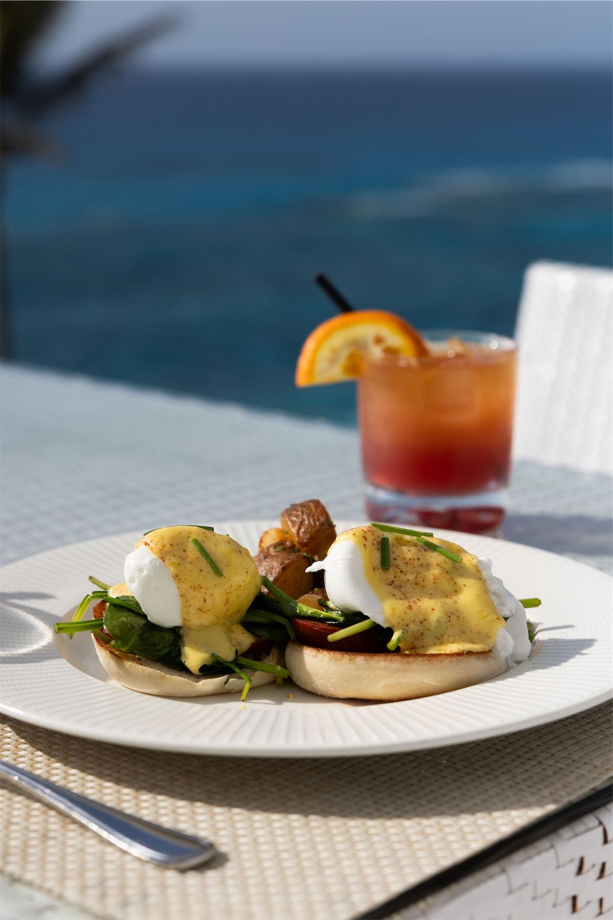 Eggs benedict served alongside a citrus cocktail at a table above the sea