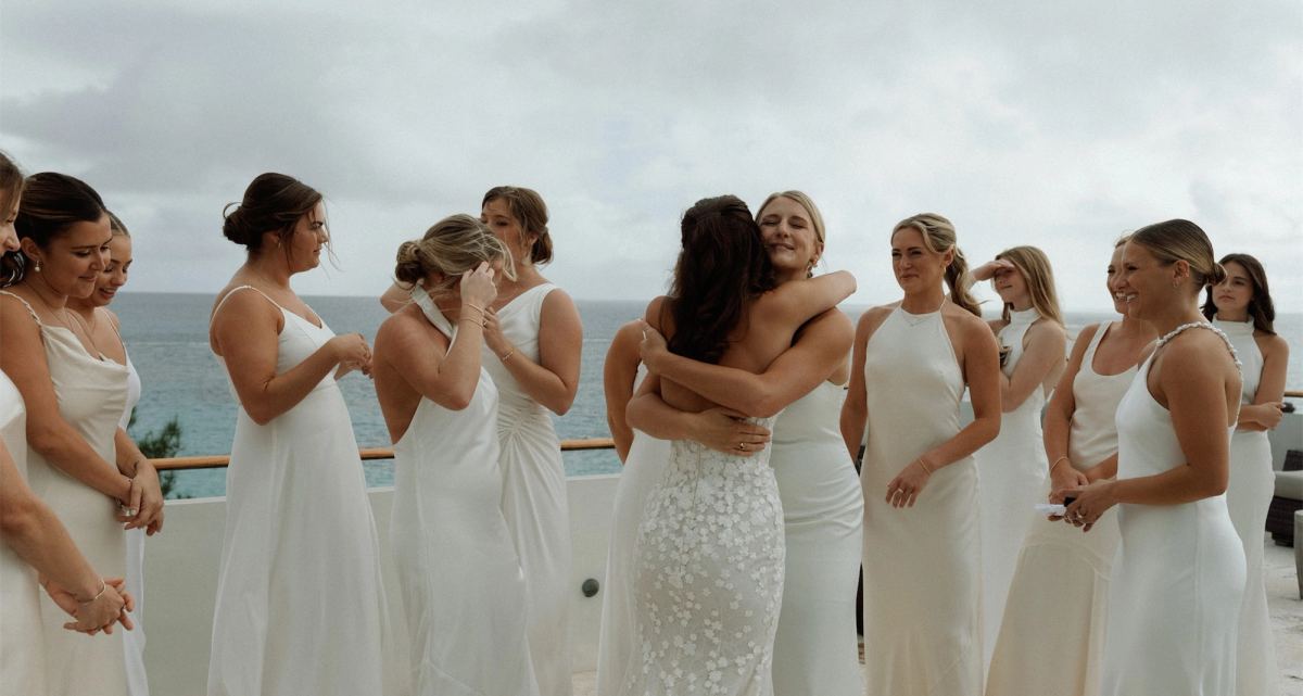 Bridesmaids in white gowns hugging the bride on a terrace above the sea