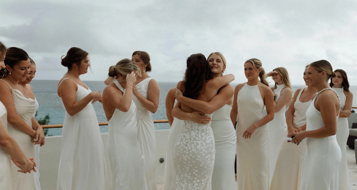 Bridesmaids in white gowns hugging the bride on a terrace above the sea