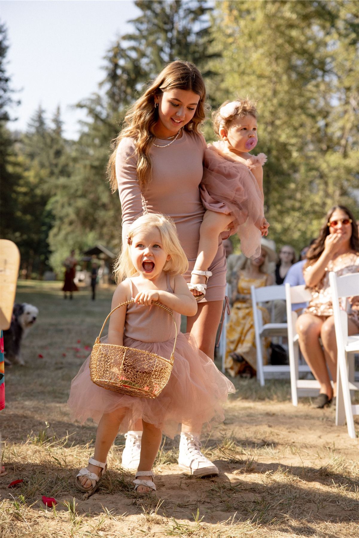 Flower girls in blush tulle walking the ceremony lawn with a guest