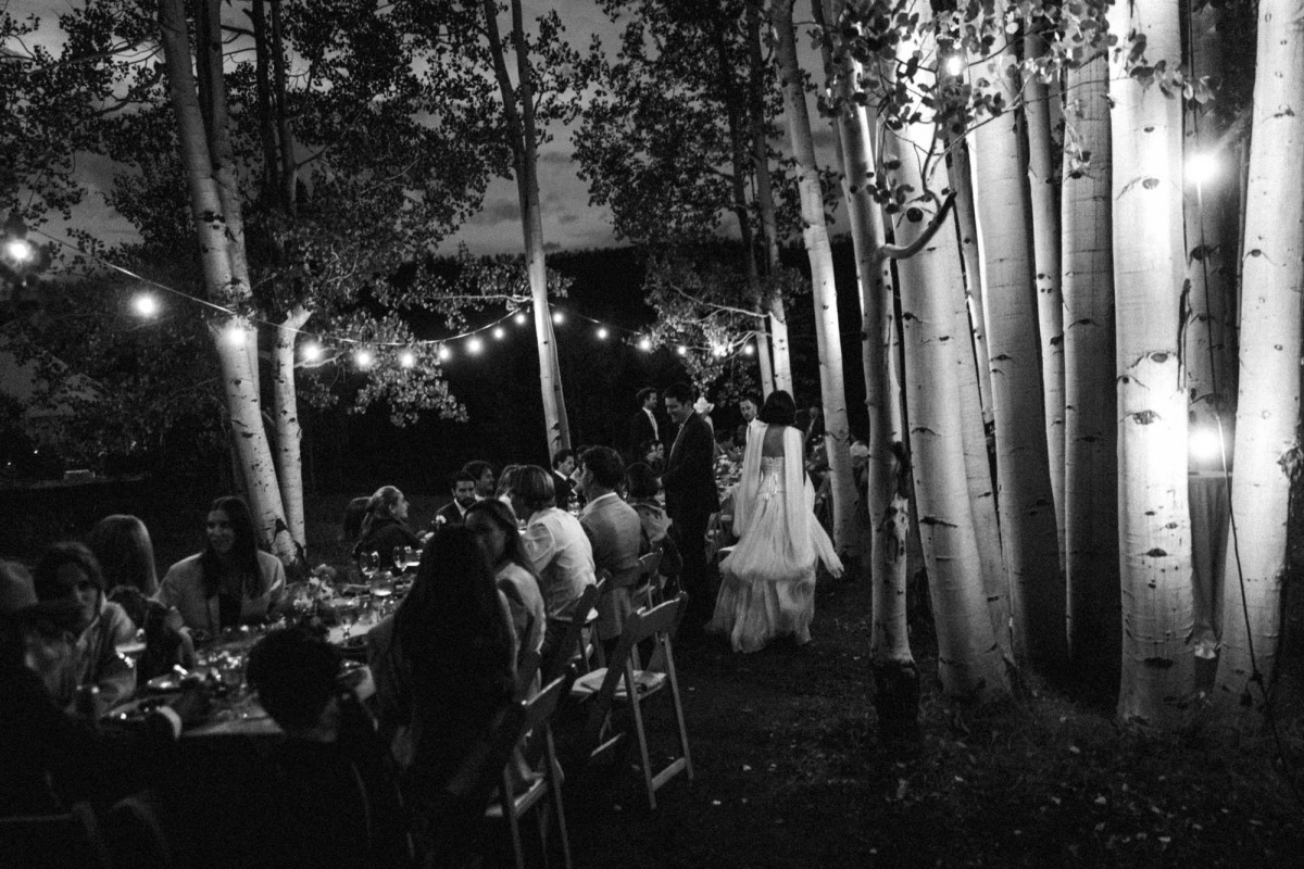 Devin walks between the tables under string lights in the aspens at a mountain ranch among the aspens, black and white
