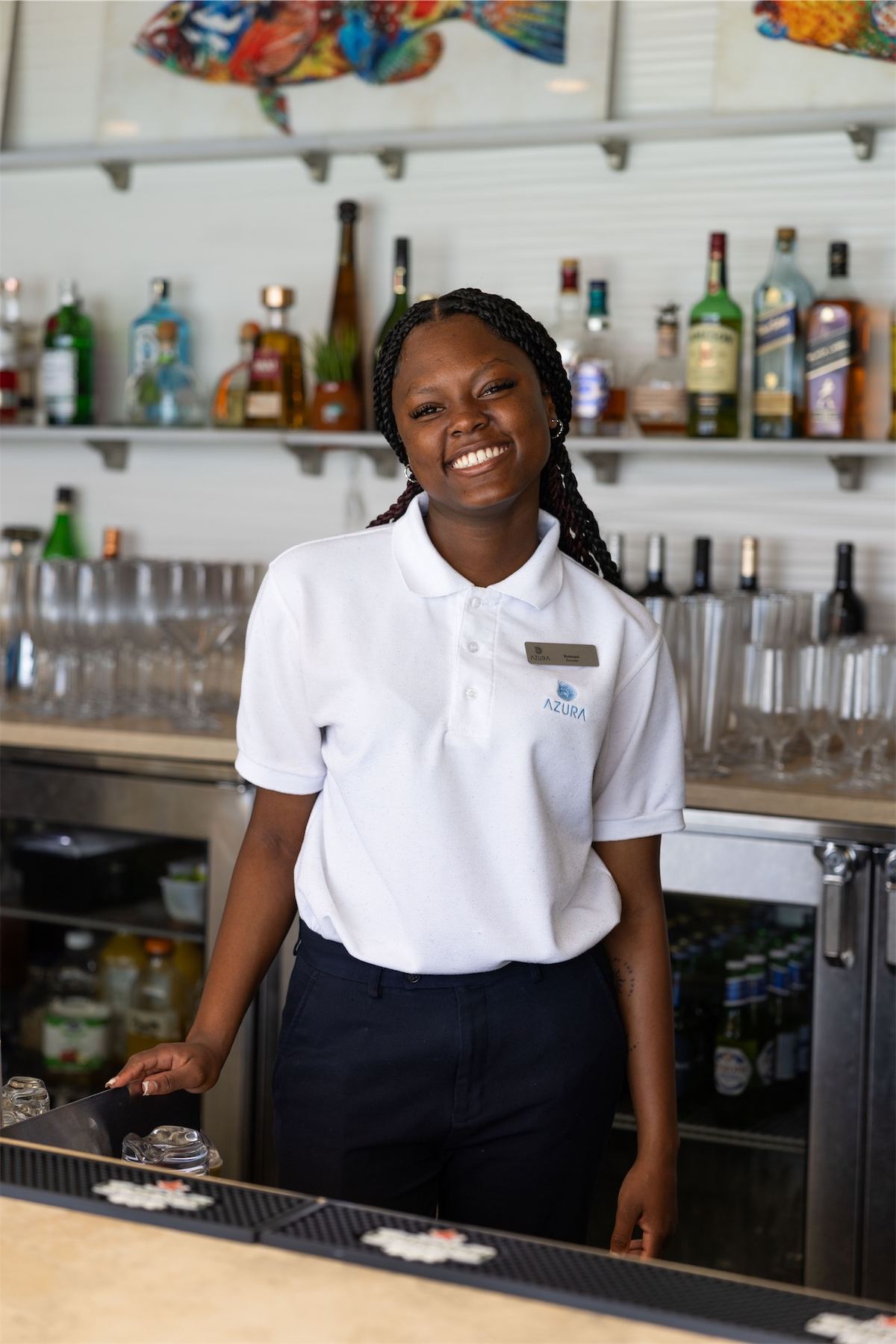 Smiling bartender in uniform standing behind a stocked bar counter
