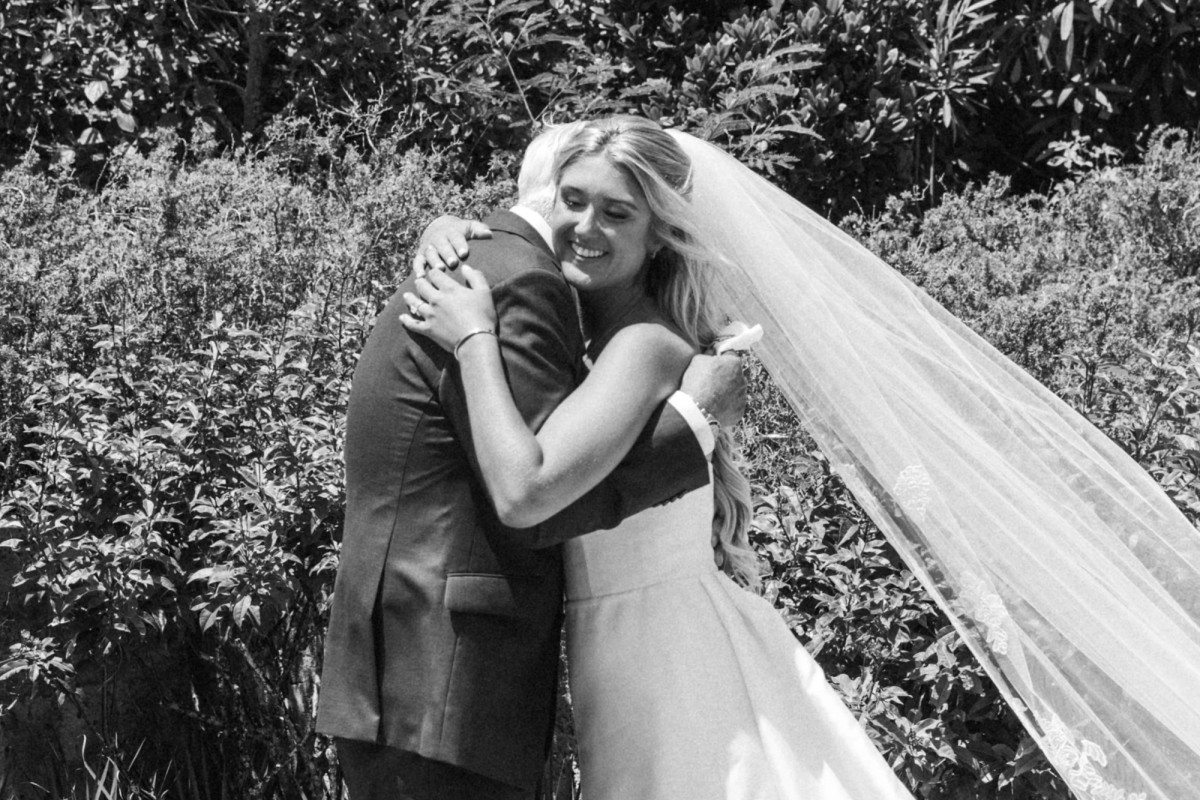 Paige hugs a loved one in the garden, her veil lifting on the breeze on Hawkins Island, Bermuda, black and white