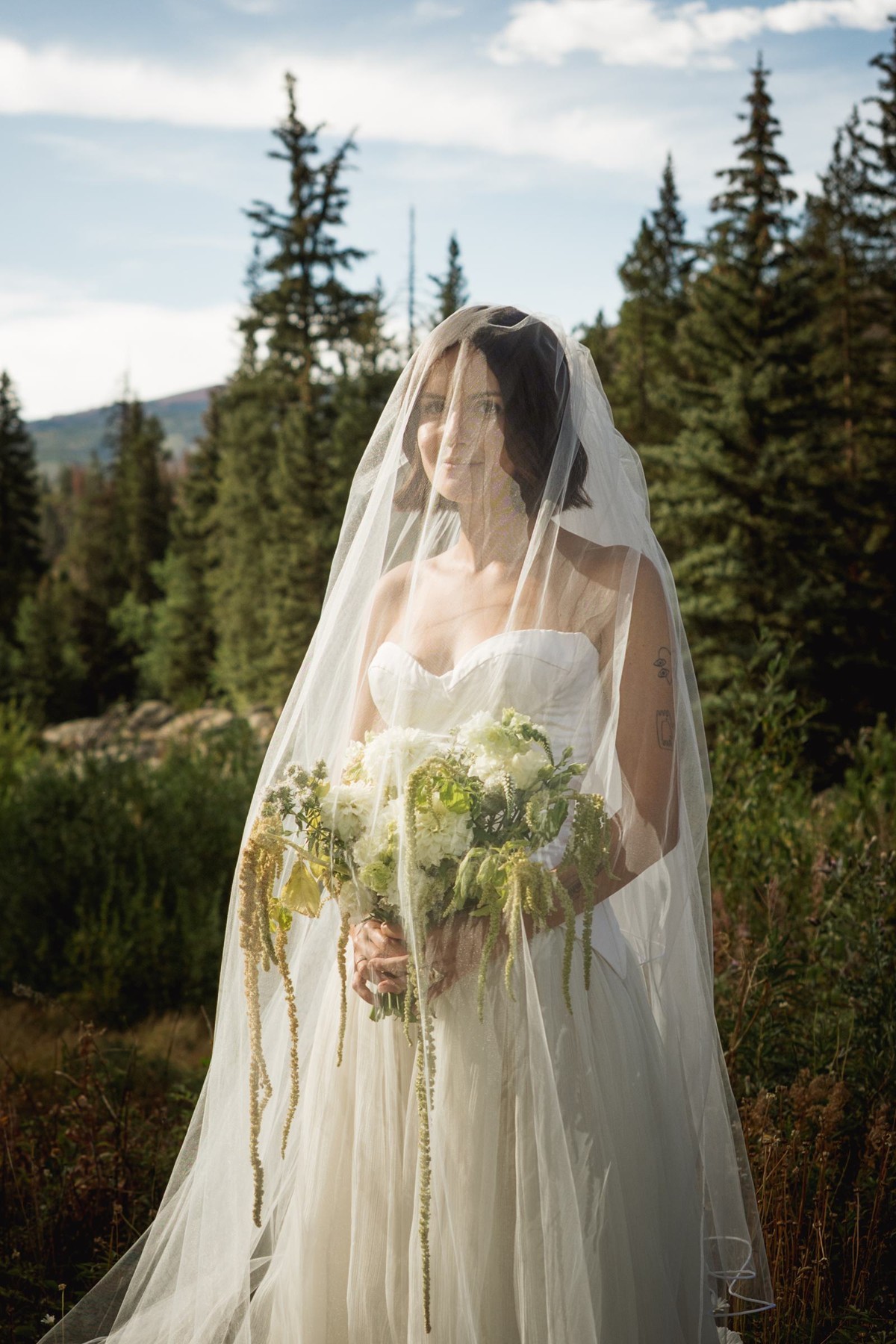 Devin in her veil holding a trailing white bouquet in the mountain meadow at a mountain ranch among the aspens