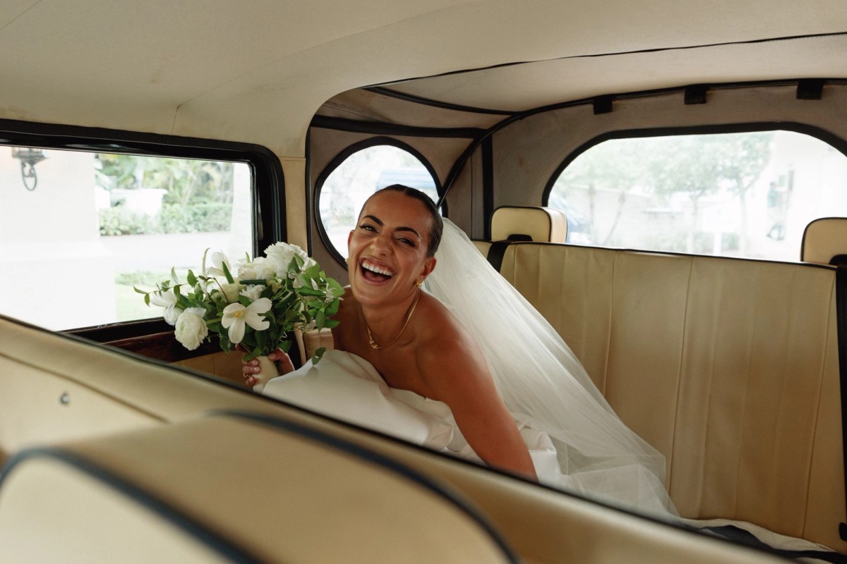 Bride laughing inside a vintage wedding car with her bouquet at Rosewood Bermuda