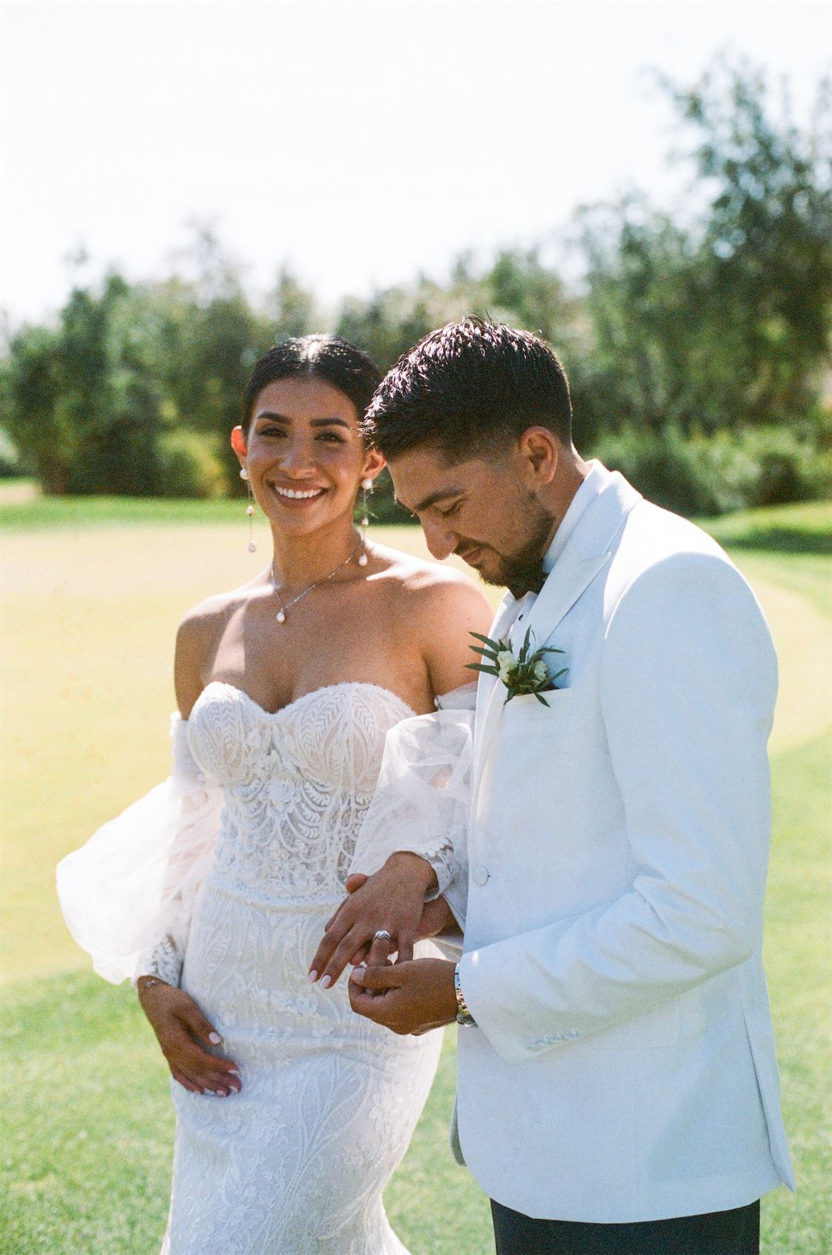 Groom in a white dinner jacket holding his bride close on the sunlit lawn