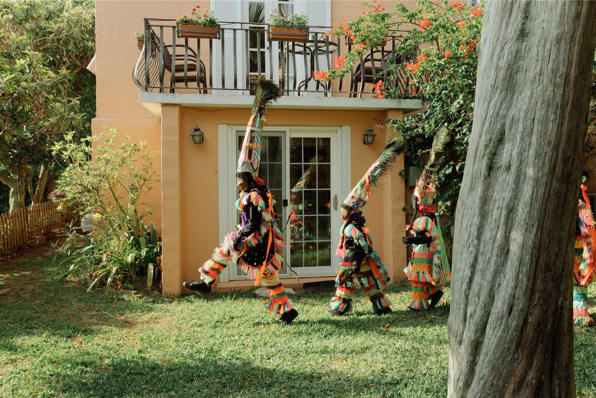 Gombey troupe dancing on the lawn outside a coral pink island house