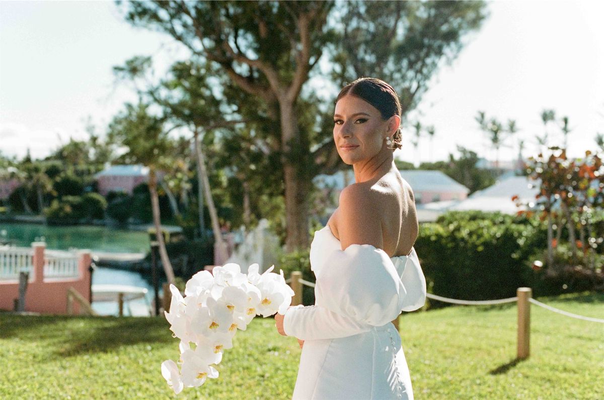 Bride holding a white calla lily bouquet on the lawn, glancing back at the camera