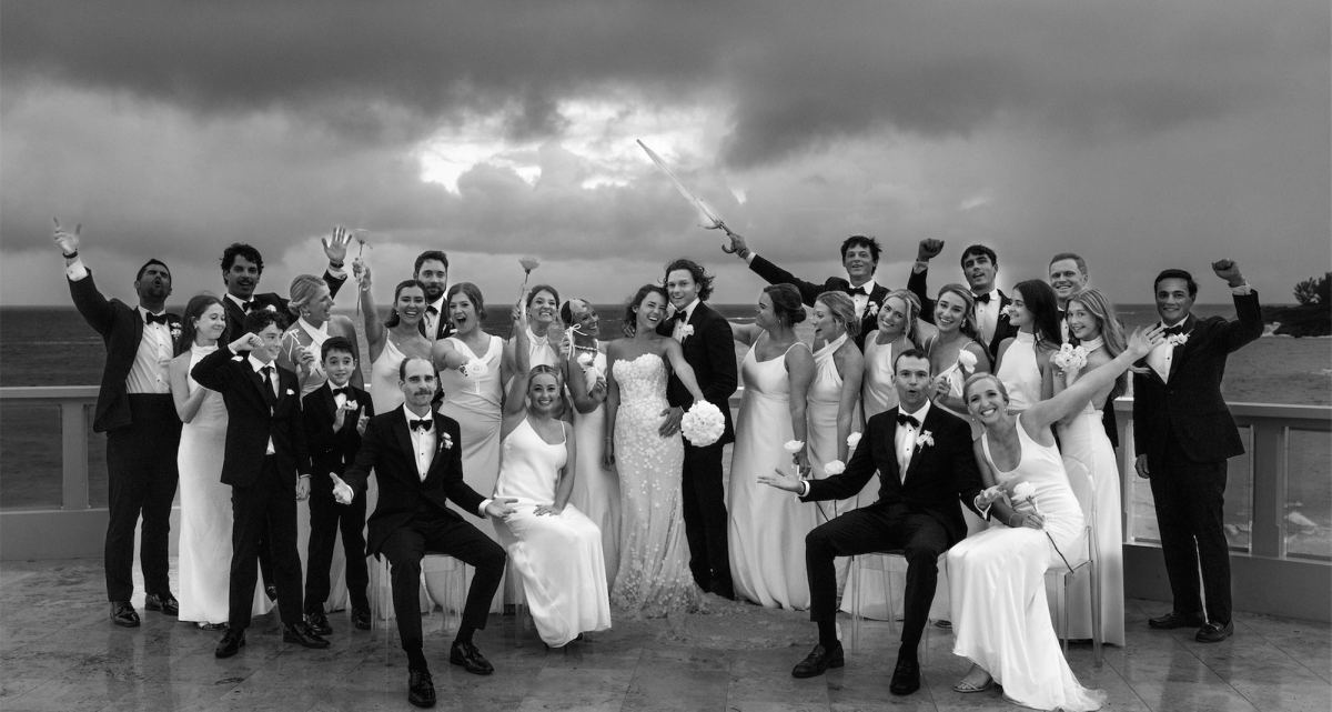 Black and white portrait of the wedding party cheering on a seaside terrace under storm clouds
