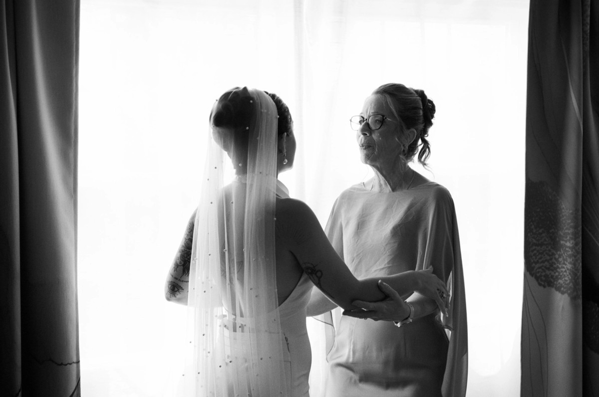 Black and white photograph of the bride's mother helping her into her veil at the window