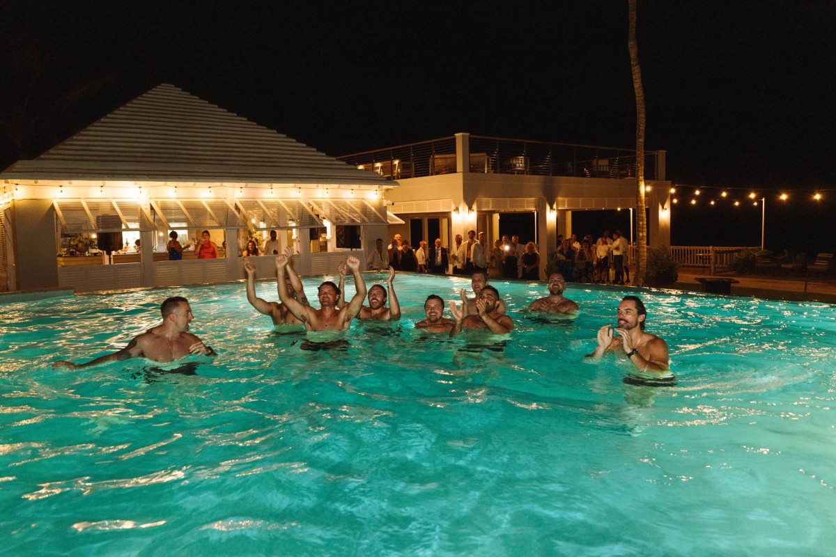 Wedding party celebrating in the glowing turquoise pool at night at Rosewood Bermuda