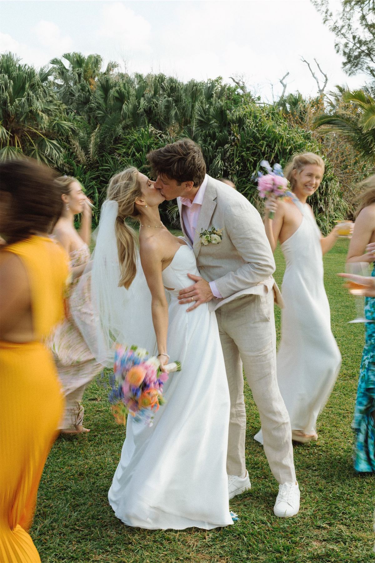 Bride and groom kissing as their bridal party circles them on the lawn