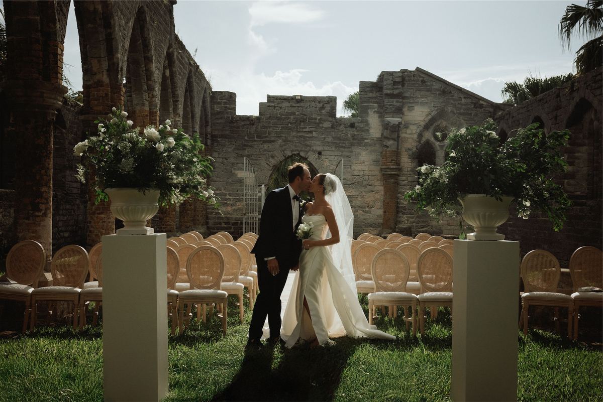 Bride and groom kissing in the ruins between urns of white flowers