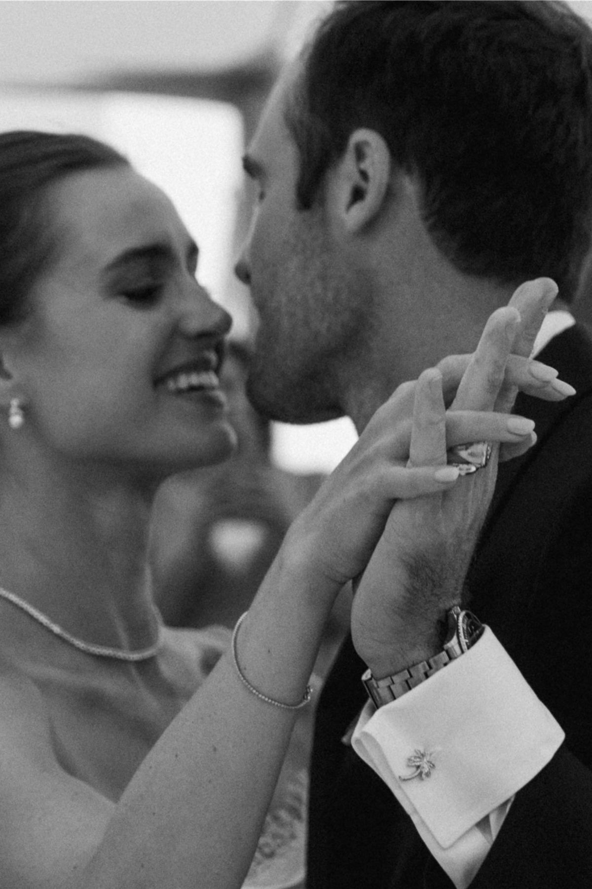 Black and white of the couple kissing, the bride's gloved hands raised