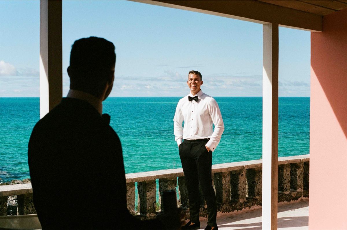 Two men in black tie talking on a shaded terrace above bright turquoise water