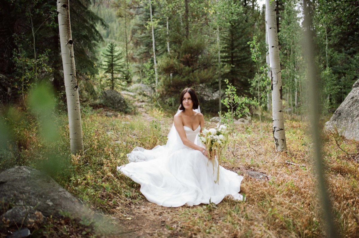 Devin sits in the wildflowers with her gown pooled around her, shot on film at a mountain ranch among the aspens