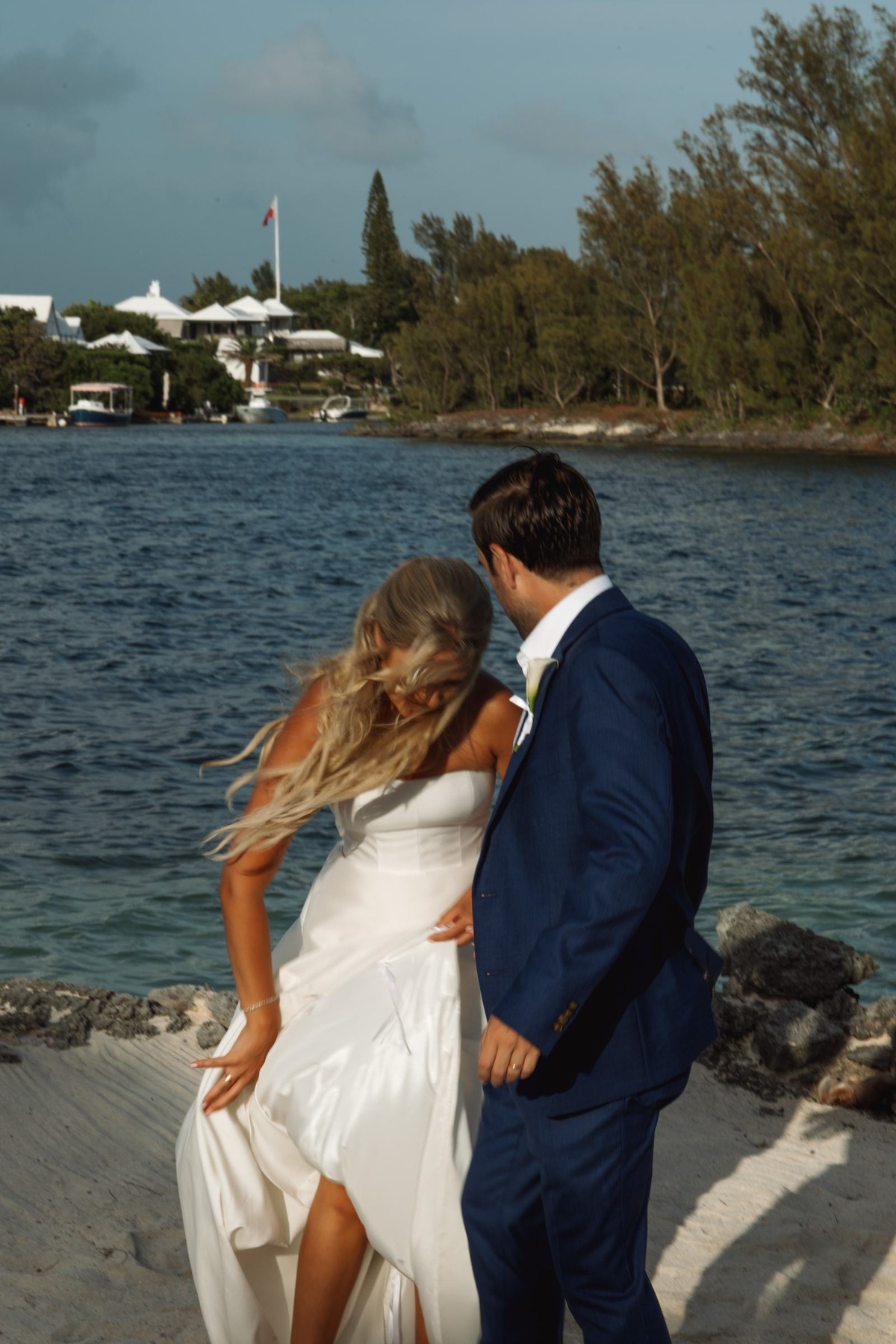 Paige and Cam laugh on the beach as the wind lifts her hair on Hawkins Island, Bermuda