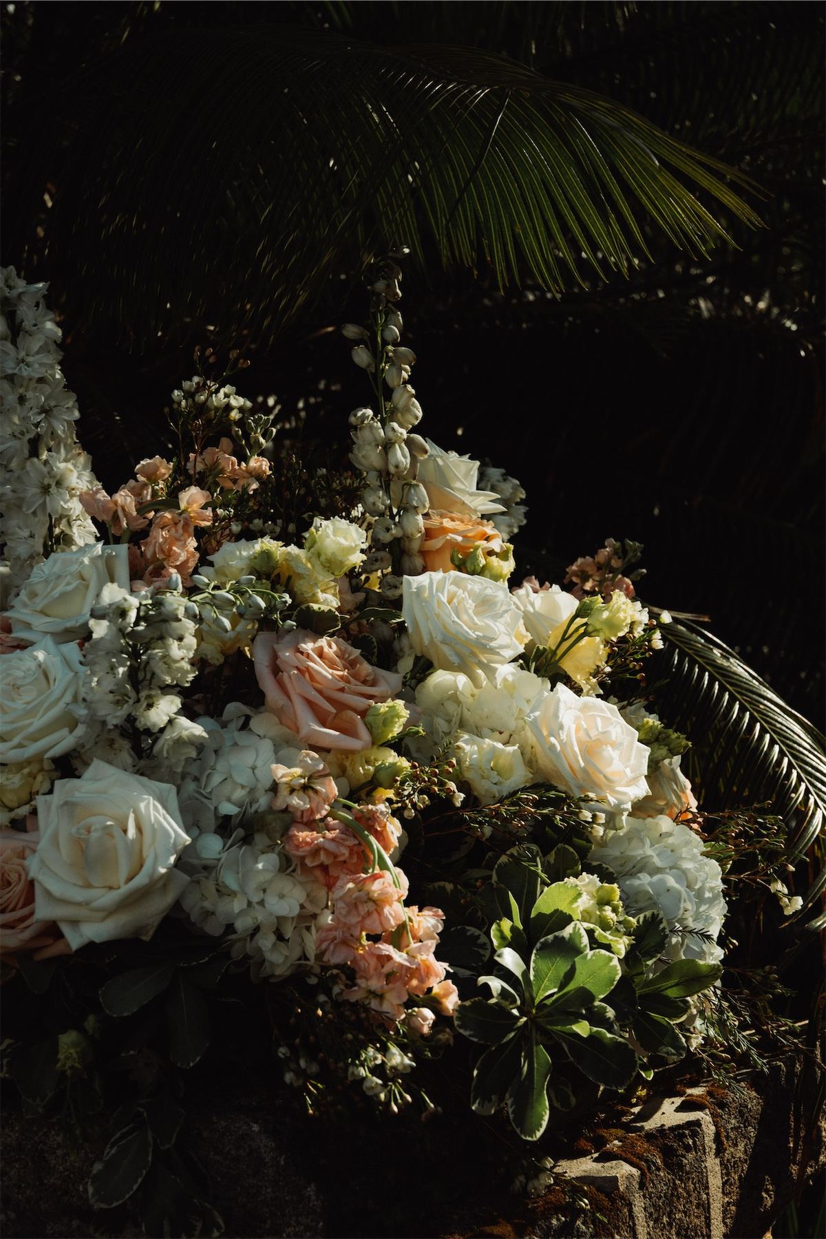 Peach and cream floral arrangement glowing against dark palm fronds at night