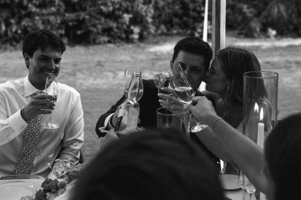 Black and white of guests clinking wine and champagne glasses across the table