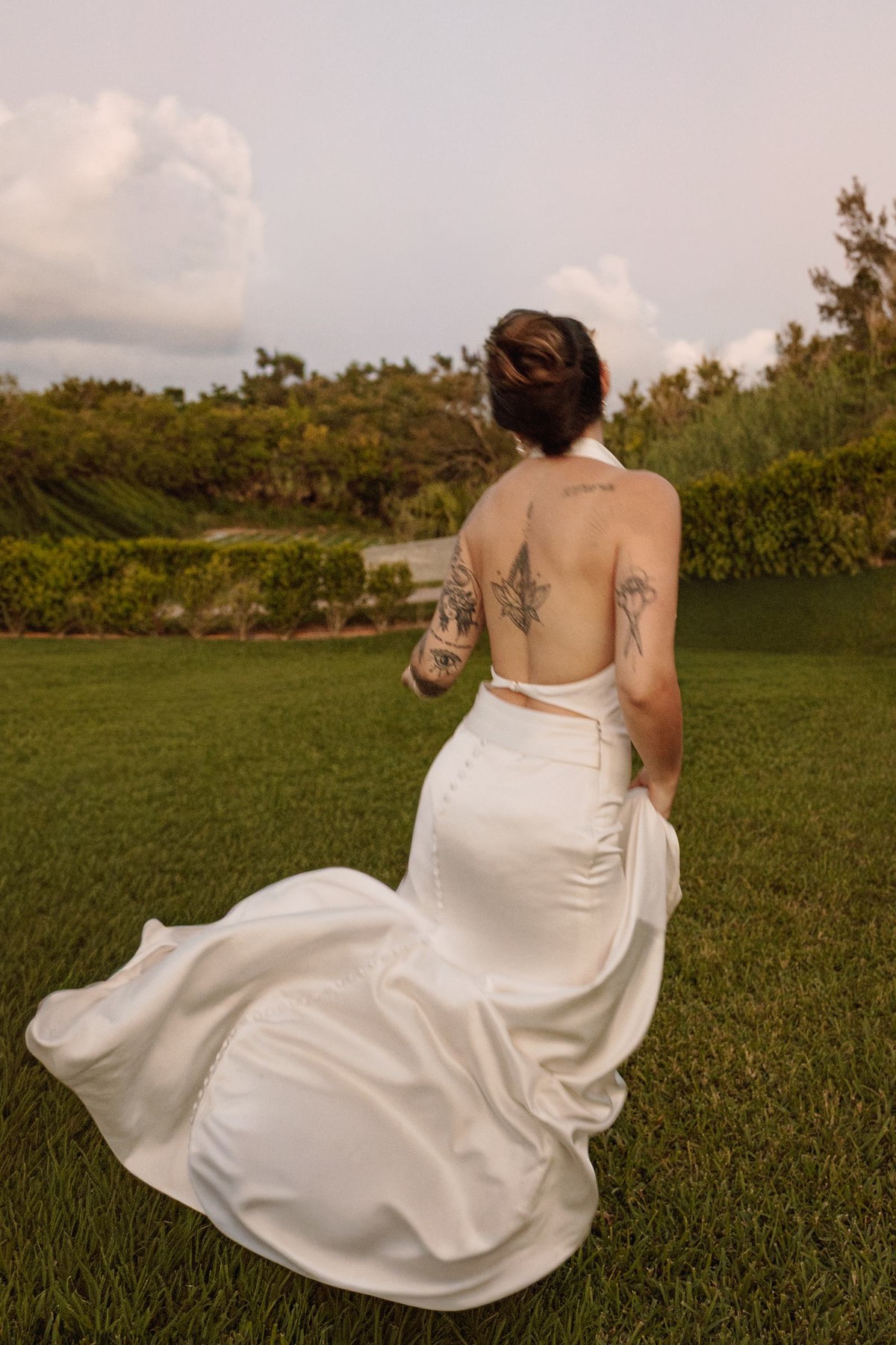 Bride from behind with her dress swirling as she walks across the lawn