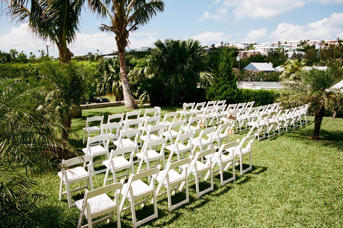 White chairs set for a Bermuda garden ceremony beneath the palms, shot on film