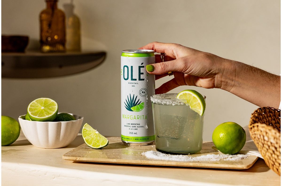 Hand setting a chilled can beside a salt-rimmed margarita on a wooden serving board