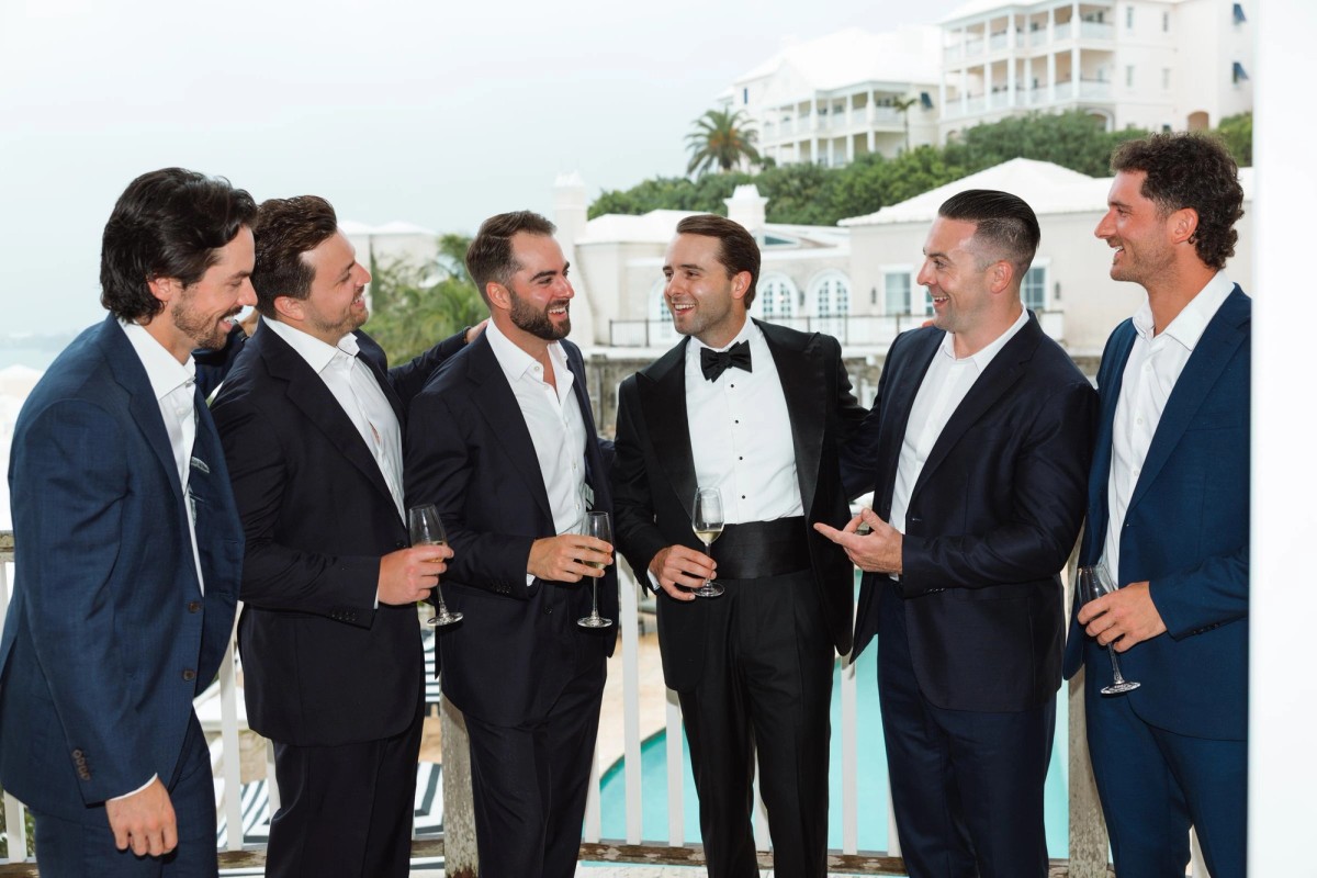 Groomsmen in navy suits sharing a laugh on the balcony at Rosewood Bermuda