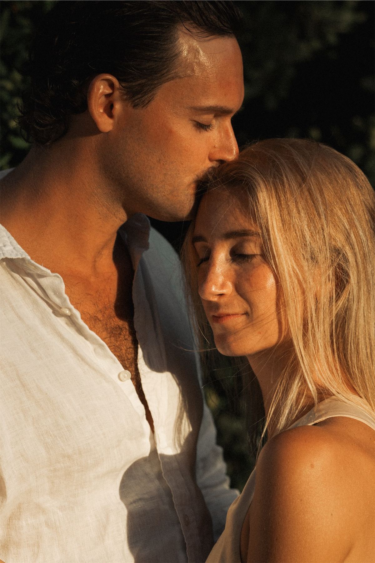 Groom kissing his bride's forehead in warm evening light