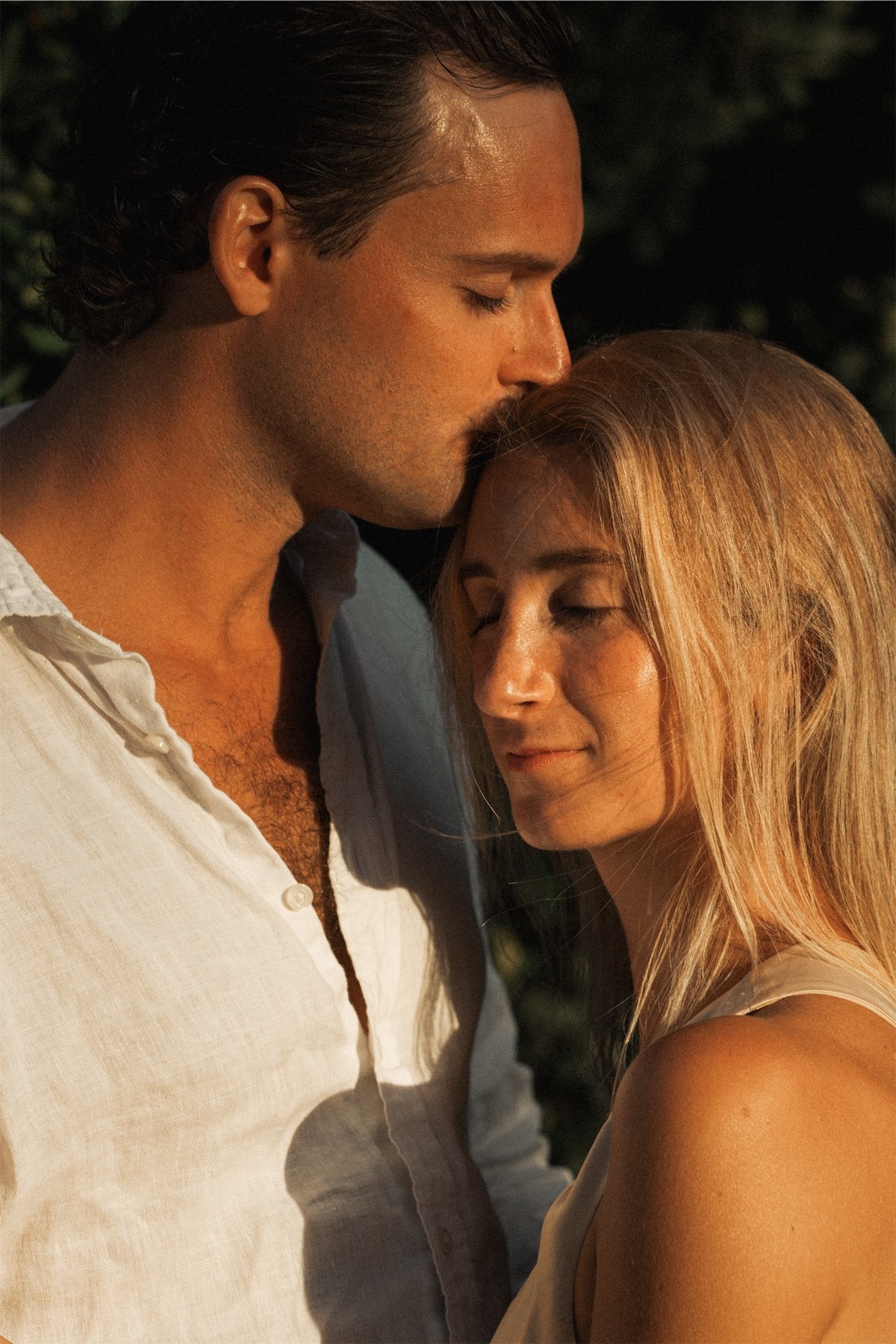 Groom kissing his bride's forehead in warm evening light