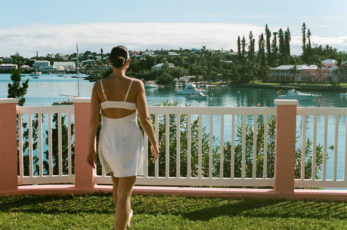 Bride in a short white dress walking toward a pink balustrade above the harbour