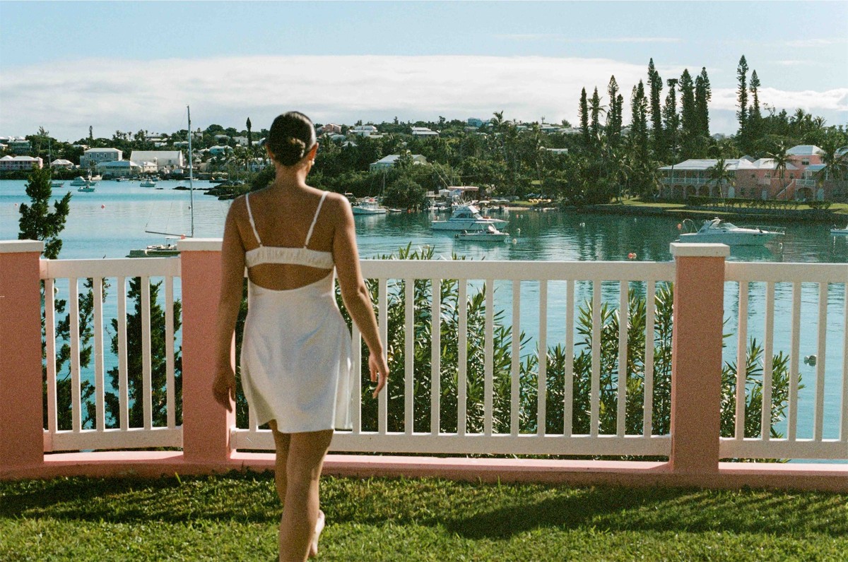 Bride in a short white dress walking toward a pink balustrade above the harbour