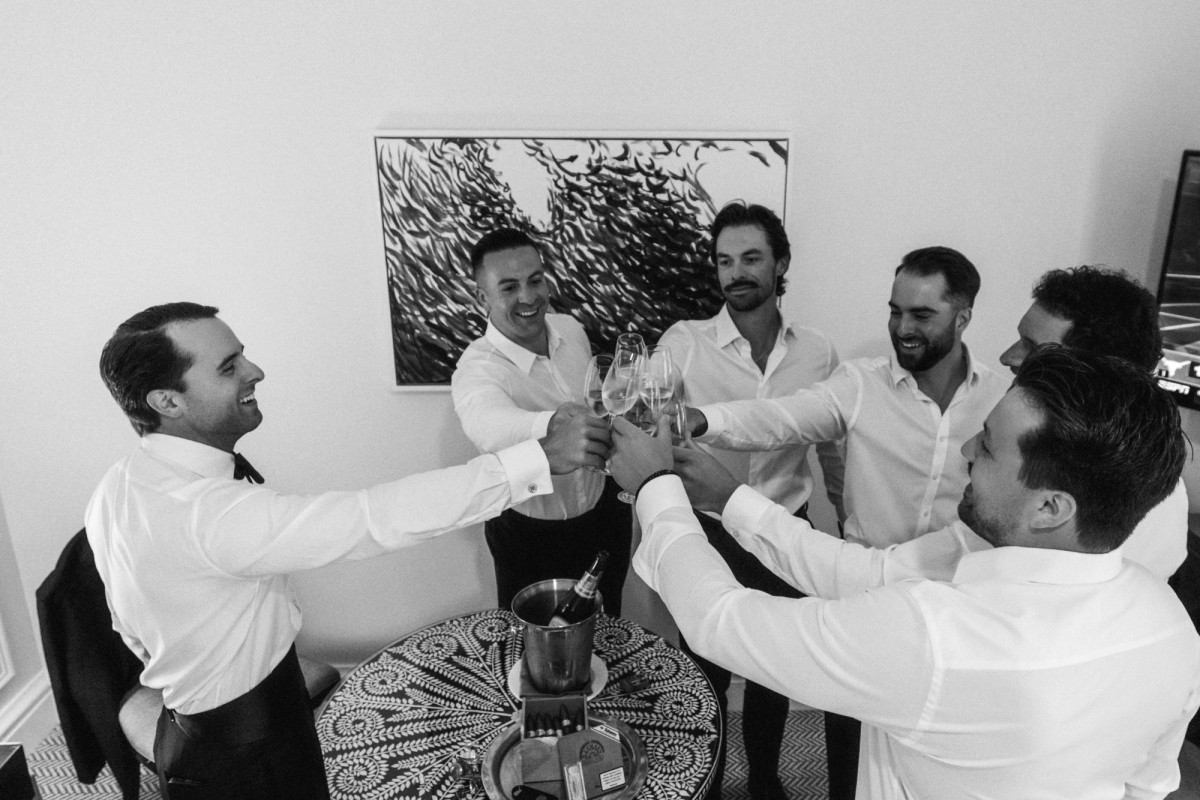 Groomsmen raising a champagne toast while getting ready at Rosewood Bermuda, black and white