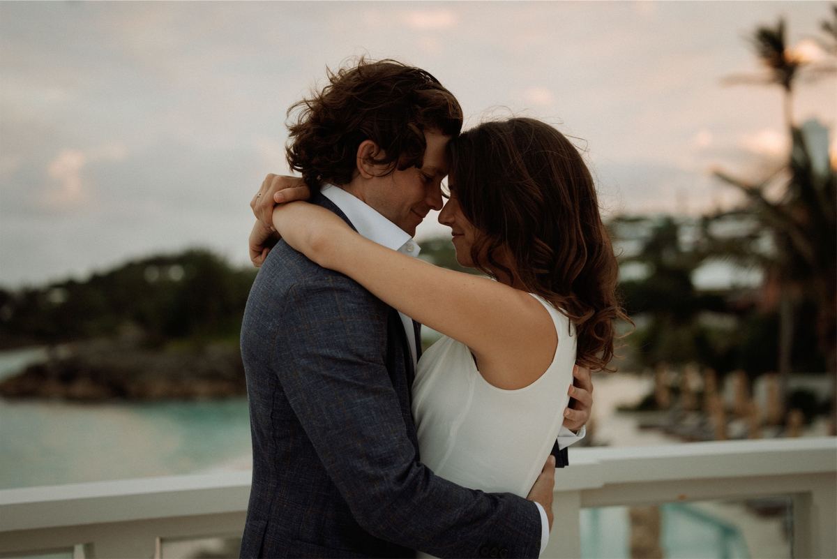 Couple embracing on a balcony high above a turquoise cove at dusk
