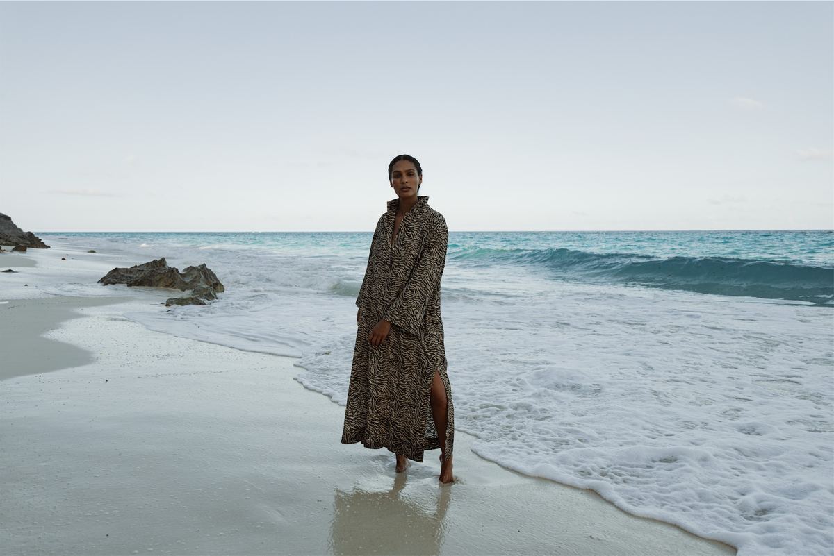 Model in a dark printed dress standing in the shallows of an empty beach