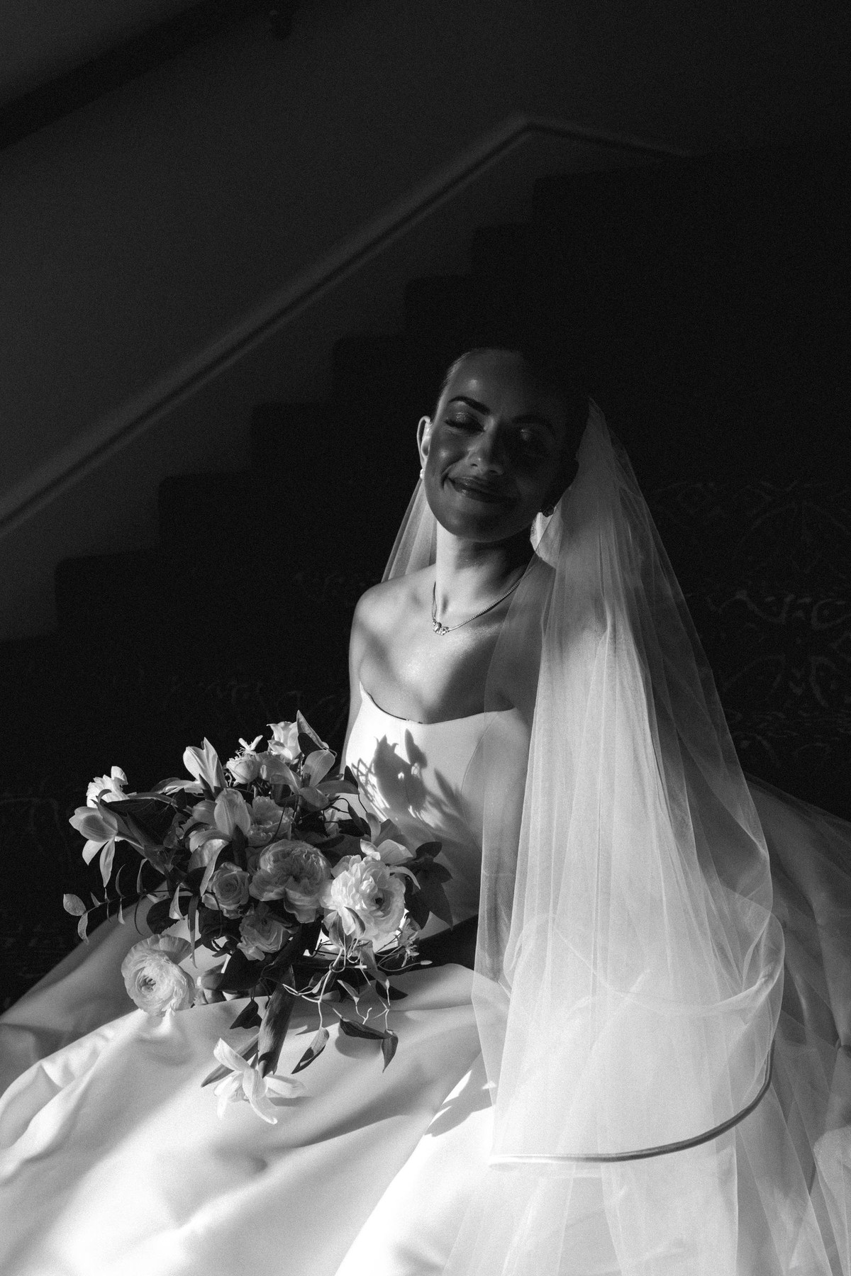 Black and white portrait of the bride smiling under her veil on a dark staircase at Rosewood Bermuda