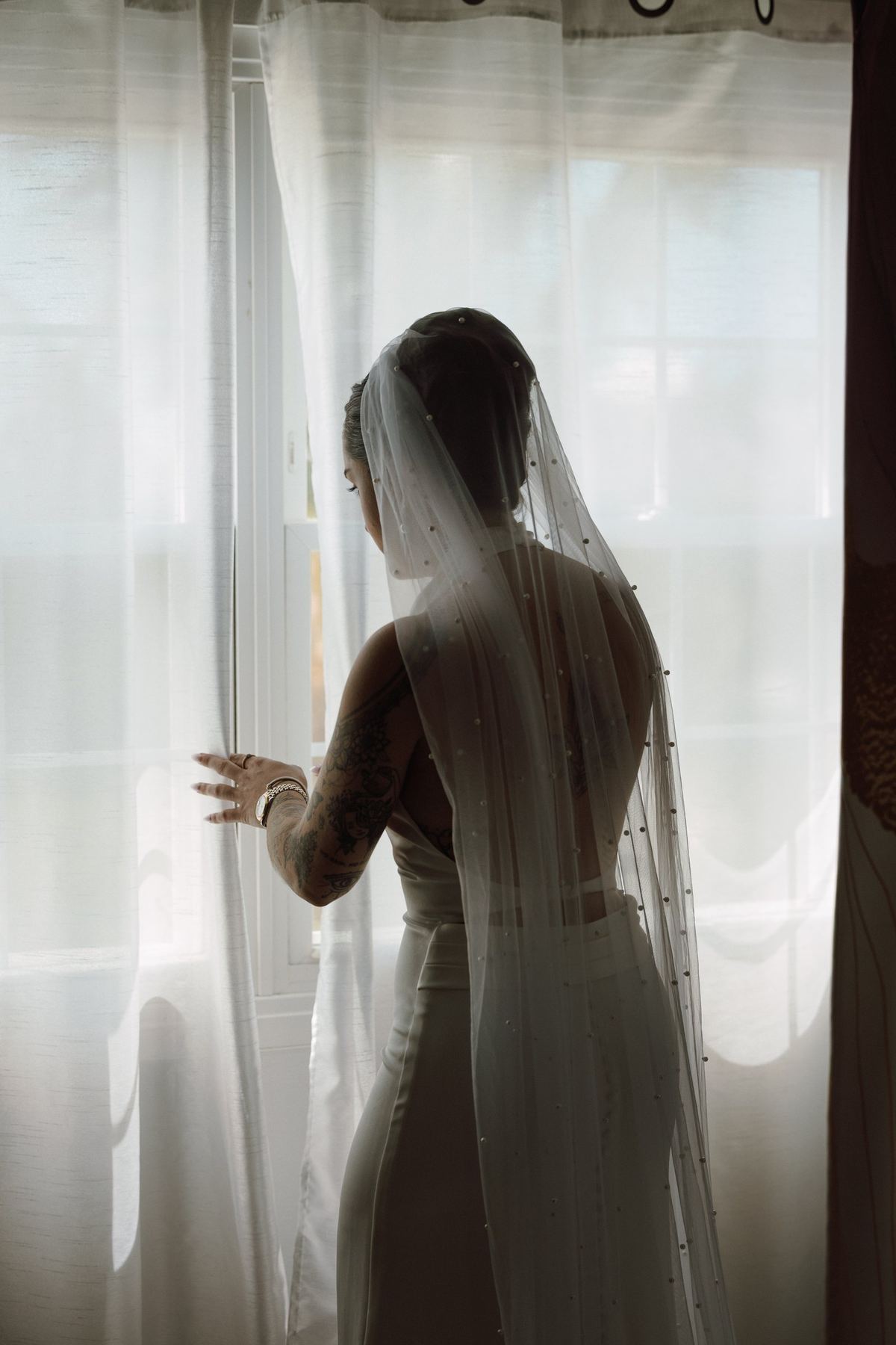 Bride standing at the window in her veil during getting ready