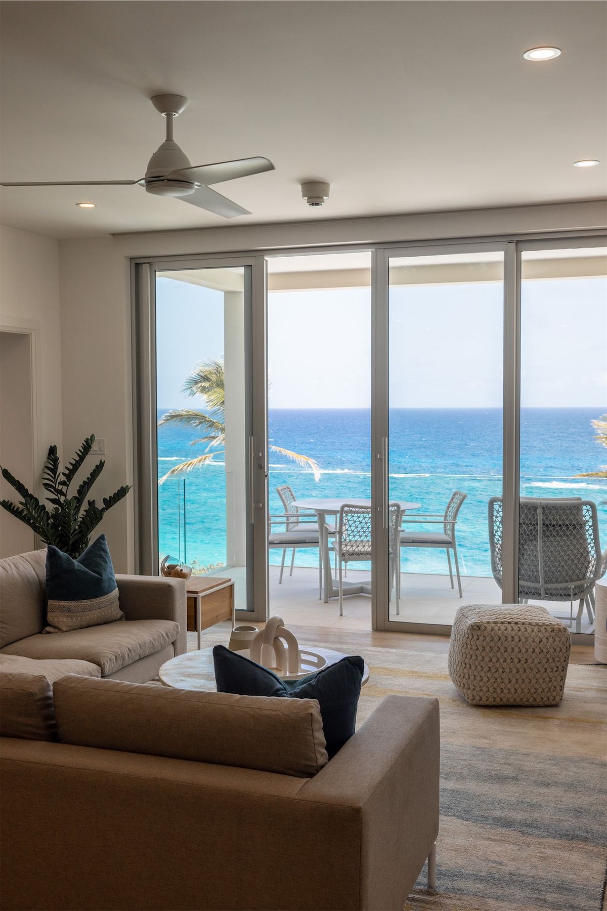Open-plan resort living room framing the ocean through full-height glass doors