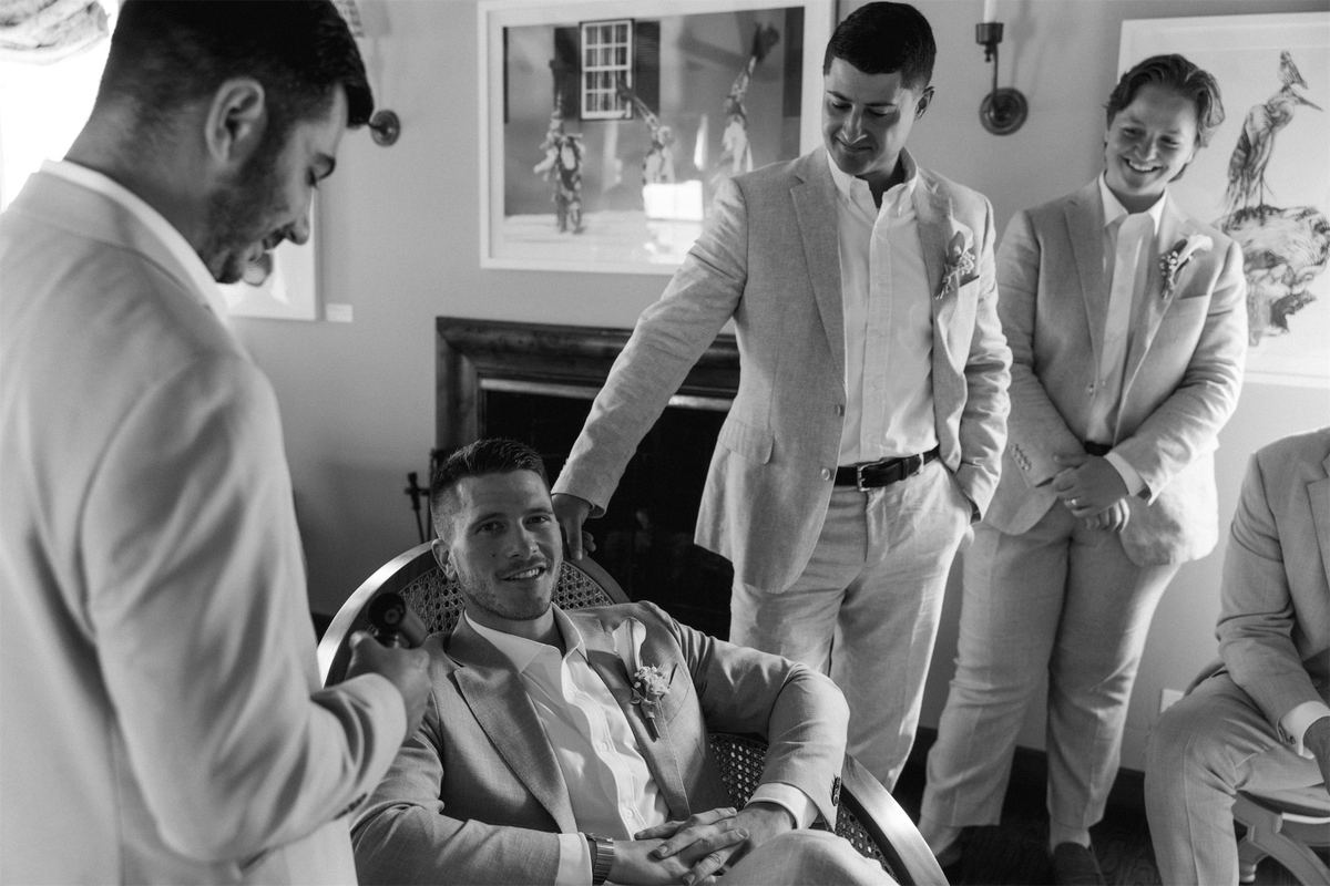 Black and white of groomsmen crowding around a friend in an armchair