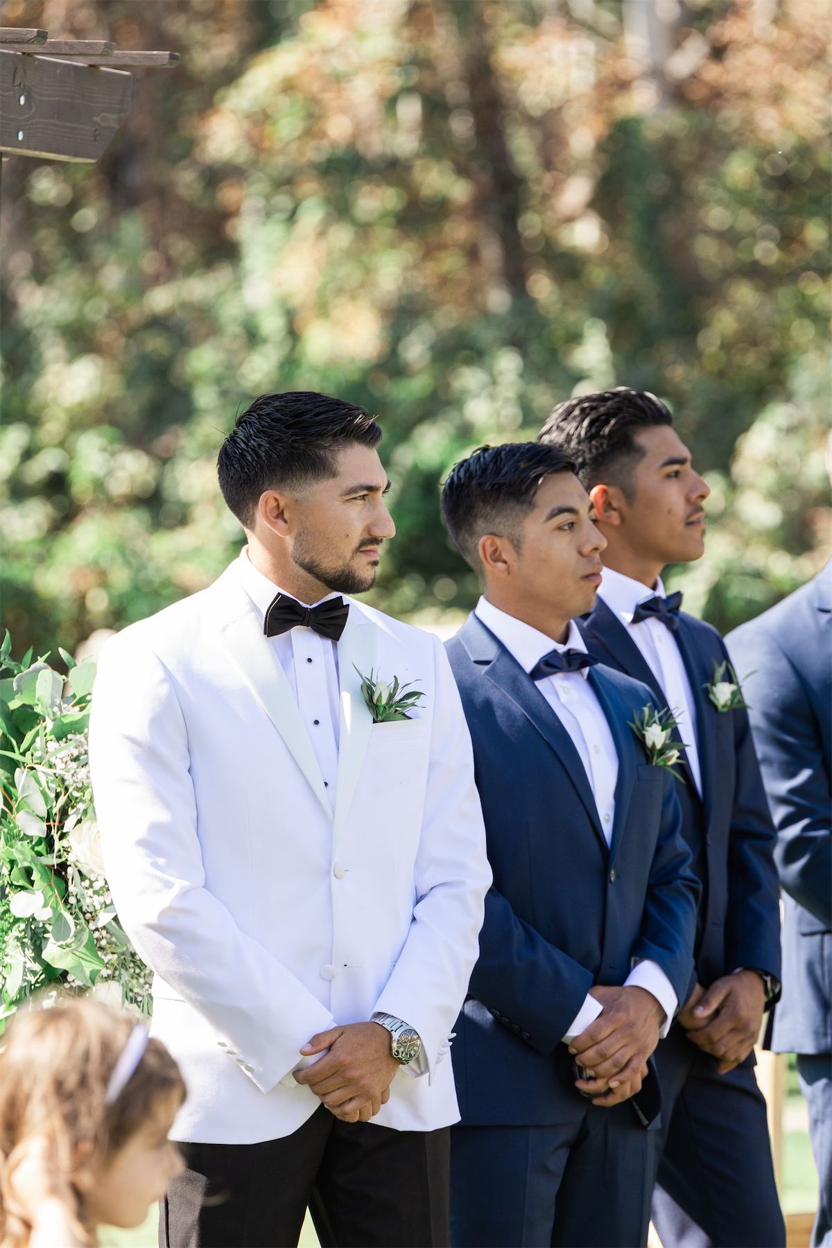 Groom waiting with his groomsmen in white and navy tuxedos at the ceremony