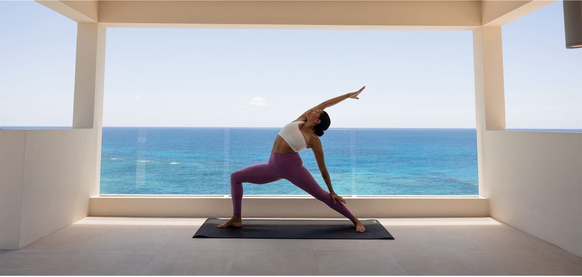 Guest holding a yoga pose on a mat in an open studio facing the ocean