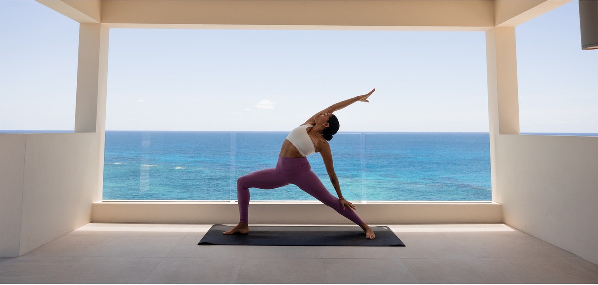Guest holding a yoga pose on a mat in an open studio facing the ocean