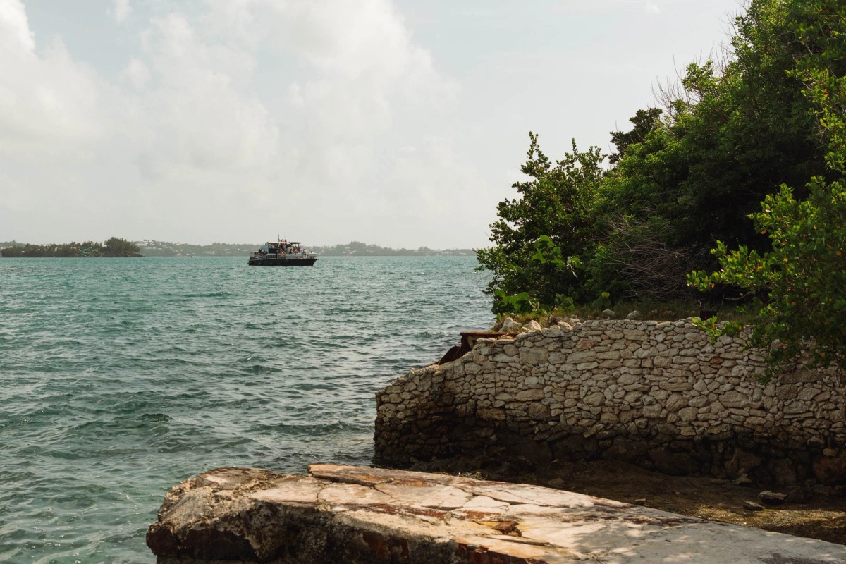 A boat crosses the turquoise bay past the rocky point on Hawkins Island, Bermuda